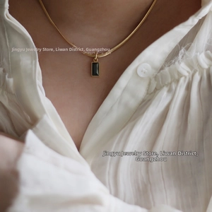 Détail d'un collier chaîne serpent dorée avec pendentif rectangulaire noir sur modèle