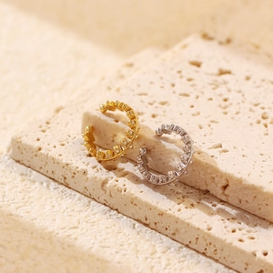 Macro shot of gold and silver ear cuffs with clear crystals on a beige stone surface
