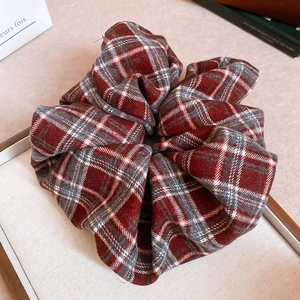 Detailed view of a red and grey plaid fabric scrunchie with soft woven texture and pleats