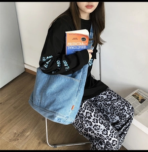 Detail of blue washed denim tote bag with soft texture and side orange label tag