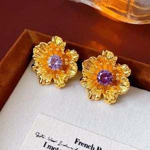 Macro shot of gold flower earrings featuring purple zircon stones with a vintage aesthetic