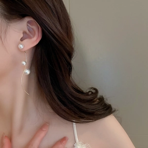 Detail of elegant S-shaped gold metal earrings with white pearls on a female model