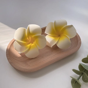 Set of two plumeria hair clips in white and yellow on a wooden tray with soft shadows