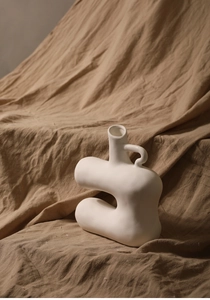 Close-up of white matte ceramic vase with unique handle on natural brown linen fabric