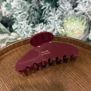 Close-up of a burgundy acetate hair claw clip with golden lettering on a wooden tray