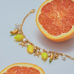 Detail of gold chain bracelet featuring colorful enamel fruit charms and white pearls