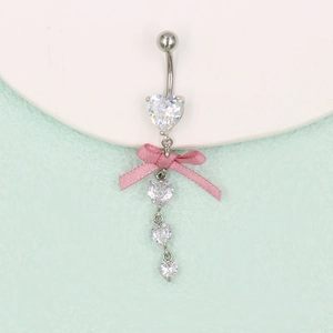 Détail macro du piercing nombril avec ruban rose et pierres de zircon en forme de cœur
