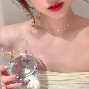 Gros plan d'un collier chaîne fine dorée minimaliste porté par un mannequin sous la lumière