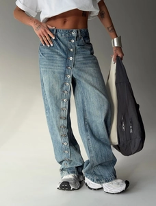 Detail of vintage washed blue jeans featuring unique metal button row on wide leg
