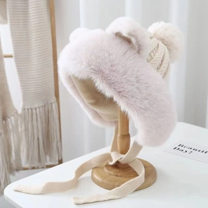 Detail of white plush trapper hat with cat ears, pom-poms and knitted tie straps