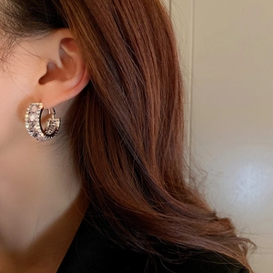 Close-up of a silver C-shaped hoop earring with shimmering zircons on a model's ear