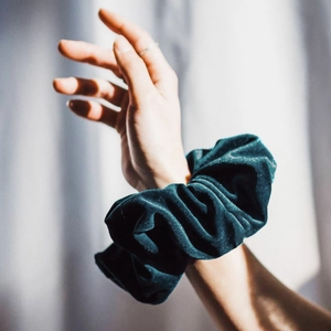 Close-up of a large dark green velvet scrunchie worn on a wrist with soft texture