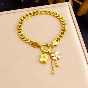 Macro shot of gold-plated curb chain bracelet featuring star square and clover pendants