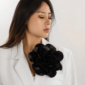 Close-up of large black fabric rose brooch on white blazer showing satin petal texture