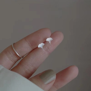 Close-up of 925 sterling silver ginkgo leaf earrings held by hand to show fine texture