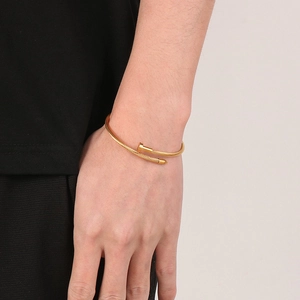Detail of a golden nail-style bracelet with a woven steel texture on a model's wrist