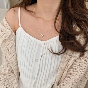 Close-up of minimalist silver bow necklace with bead pendants on a model wearing white