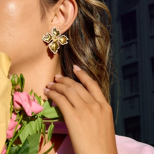 Close-up of 18K gold stainless steel flower earrings with white enamel on model