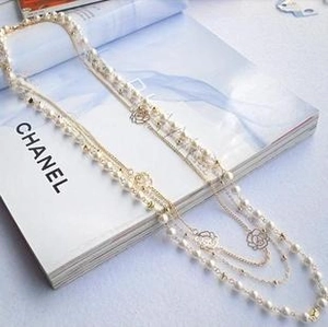 Detail of layered gold chain and white pearl necklace featuring hollow rose flower pattern