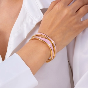 Close-up of three-piece pink enamel and gold-plated wavy bangles worn on a wrist