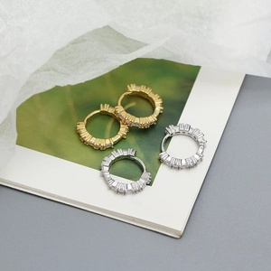 Dettaglio di orecchini a cerchio in argento e oro con cristalli su carta bianca