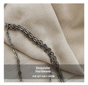 Close-up of polished silver metal chain strap detail on a beige corduroy texture background