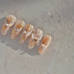 Detailed close-up of nude pink nail tips featuring 3D butterfly, pearls, and glitter