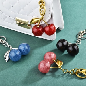 Sparkling resin cherry keychain in four colors displayed on a green surface with a bag