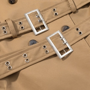 Detailed shot of khaki trench coat featuring silver square buckles and resin buttons