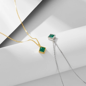 Close-up of square emerald zircon pendants in gold and silver finishes on fine chains