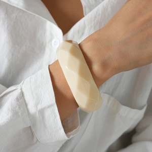 Detail eines minimalistischen, geometrischen Armreifs aus Acryl in Creme am Handgelenk