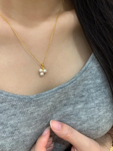 Close-up of golden necklace with three round pearls and a zircon pendant on a model