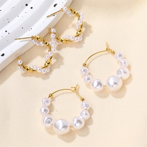 Detail of twisted gold earrings and gradient pearl hoops on minimalist background