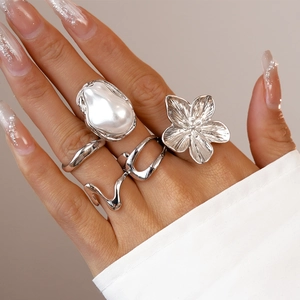 Detail von Silberringen mit Perlenblumen und geometrischen Wellen an einer Modelhand