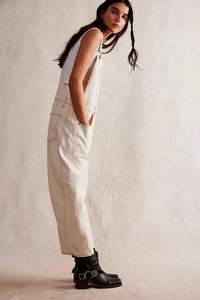Side view of woman wearing cream denim dungarees with white vest and black biker boots