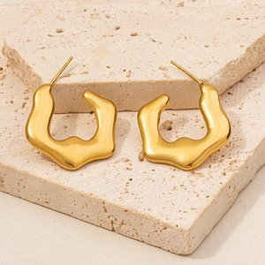 Close-up of golden 304 stainless steel earrings with wavy texture on beige stone
