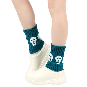 Detailed close-up of dark green knitted leg warmers featuring white skull patterns