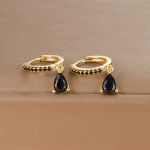 Macro detail of gold hoop earrings featuring black zircons and pear-shaped drop stones
