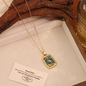 Détail d'un collier doré vintage avec pendentif oiseau en émail vert sur velours blanc
