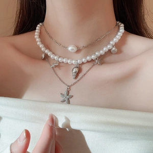 Detail of layered necklace featuring starfish, conch pendants and white pearls on a model