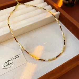 Détail du collier de perles fleurs avec accents dorés et pierre brune dans une boîte