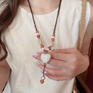 Gros plan d'un pendentif cœur en céramique avec cordon tressé et perles au cou