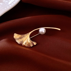 Makroaufnahme der vergoldeten Ginkgo-Brosche mit feinen Texturen und einer Glanzperle