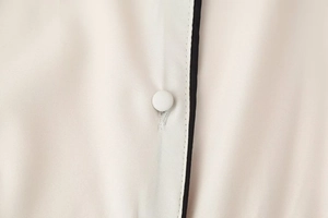 Détail macro du bouton de robe blanc cassé avec passepoil noir et texture de tissu tissé