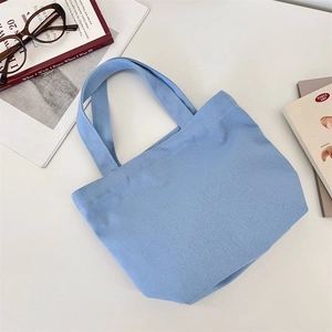 Macro della borsa da pranzo in tela blu su una scrivania con occhiali e libri, stile