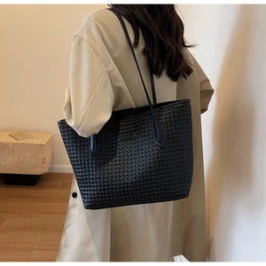 Fashionable black woven tote bag shown on a model in a stylish beige trench coat