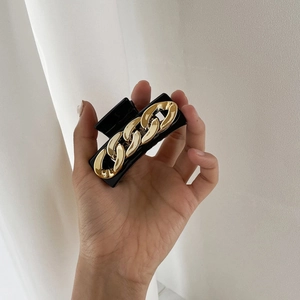 Minimalist black hair claw clip with golden chain design held against a white background