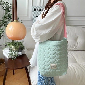 Quilted green shoulder bag with heart pattern and pink strap for women on sofa