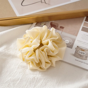 Detailed shot of yellow chiffon scrunchie with lace edges and small pearls on linen