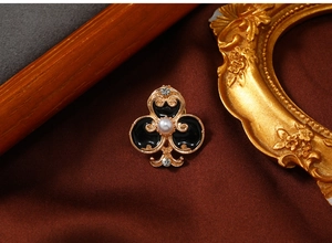 Macro view of vintage gold clover brooch with black enamel, pearl, and rhinestone accents